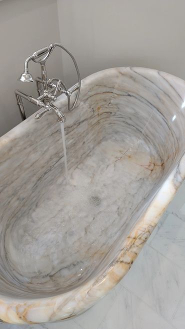 Elegant marble bathtub with running water and chrome faucet.