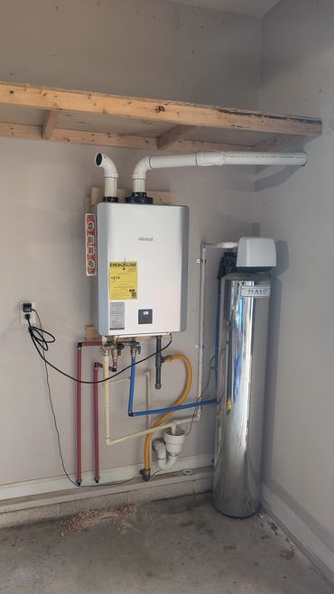 A modern water heating and filtration system installed on a wall with multiple pipes and a wooden shelf above.