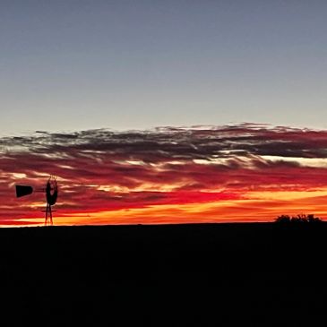 Silhouette of a windmill against a vibrant red and orange sunset sky.