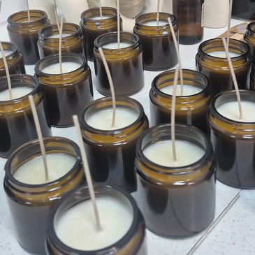 Rows of handmade candles in brown glass jars with neutral-toned decor in the background.