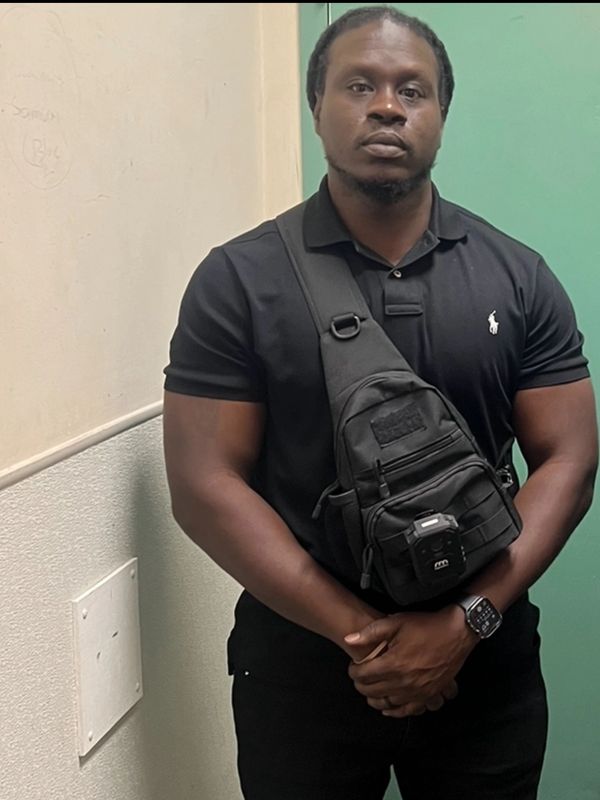 Man in black polo shirt with a crossbody bag and watch.