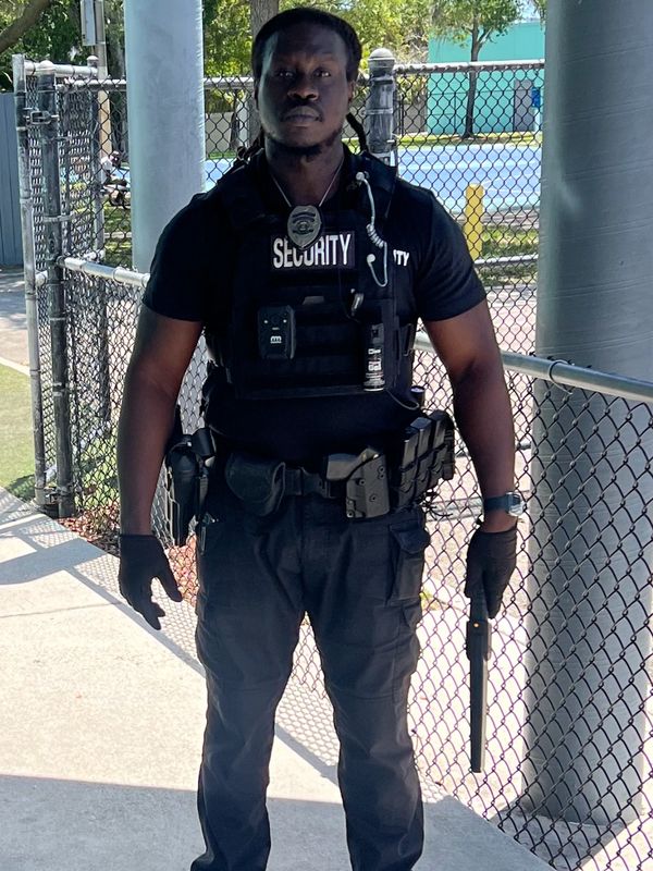 Security guard in full uniform standing outdoors with baton.