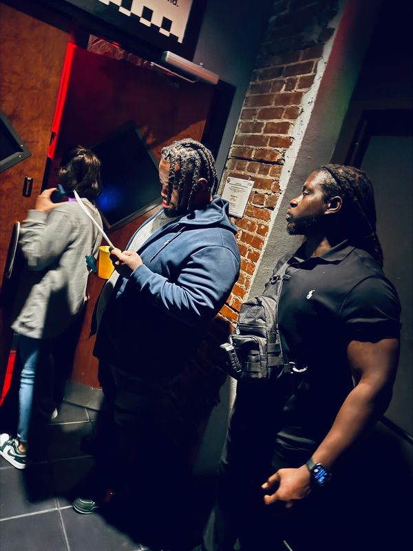 Three people near a brick wall and door, one reading a paper.