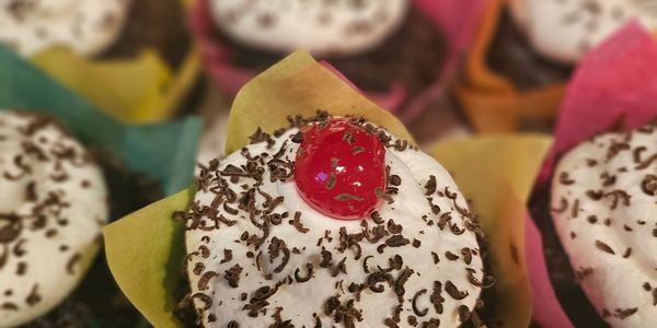 Chocolate cupcakes with whipped cream, chocolate shavings, and cherries on top.