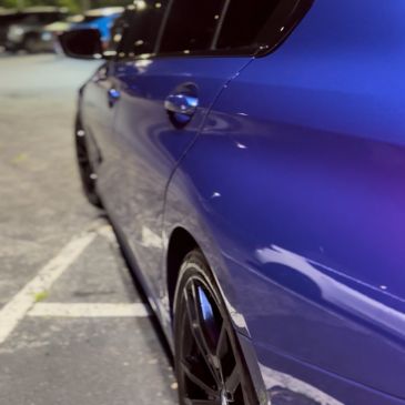 Close-up of a shiny blue car's side and wheel at night.