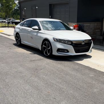 White Honda sedan parked on a sunny street near a building.