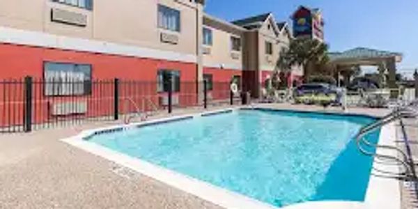 Outdoor swimming pool beside a hotel building under clear sky.