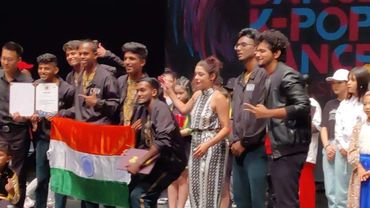 Group of young people celebrating with an Indian flag and certificate on stage.