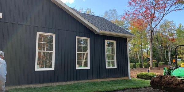 Newly laid sod on the side of a dark blue house under a clear sky.