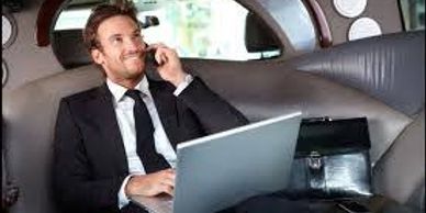 Man in suit on phone with laptop in limousine.