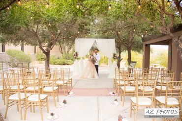 Bride and groom standing under a decorated white arch at an outdoor wedding.