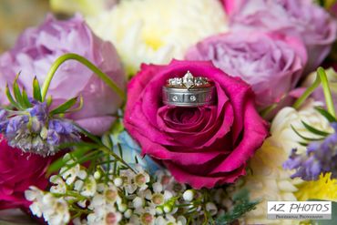 Wedding rings nestled in a vibrant pink rose surrounded by colorful flowers.
