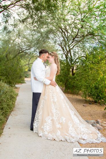 Bride and groom embrace outdoors on a tree-lined path.