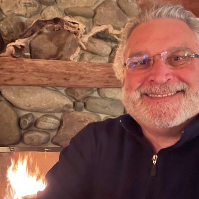 Smiling man with glasses by a cozy stone fireplace.