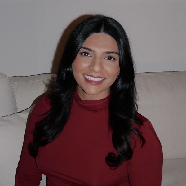 A woman with long black hair sitting on a couch, smiling warmly.