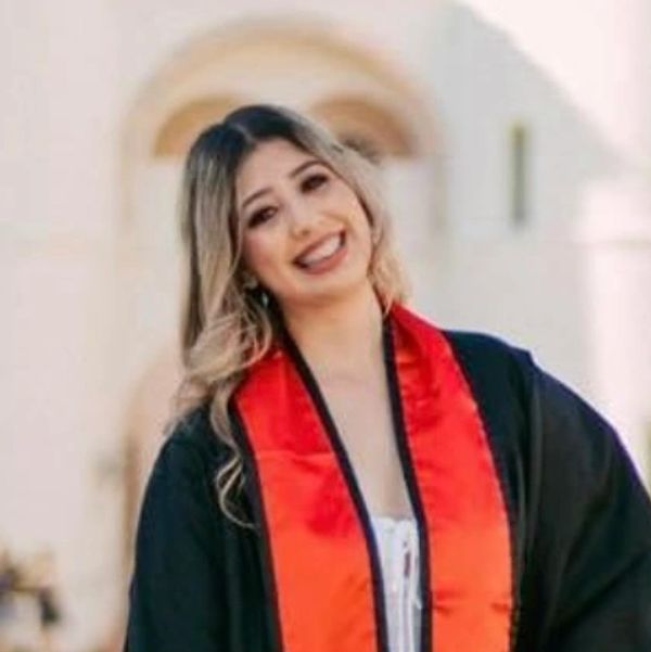 Smiling graduate in black gown and red stole.