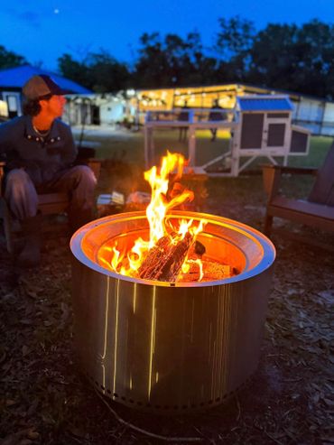 One of the dinner party guests sitting by the fire pit at night with a lit-up barn behind.
