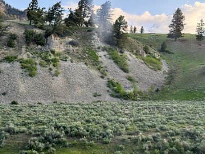 Rocky hillside with greenery and trees under a partly cloudy sky.