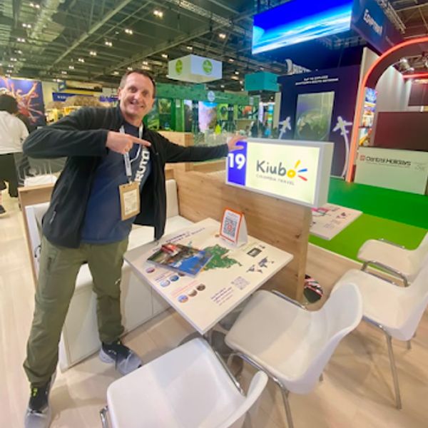 Mann zeigt begeistert auf ein Kiubo-Reiseschild an einem Messestand.
