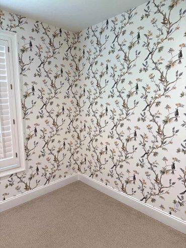 Chinoiserie bird and branch wallpaper in a bedroom corner beside a shuttered window