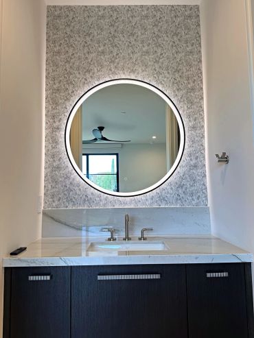 Grey scallop wallpaper behind a round backlit mirror over a navy vanity in an Arizona bathroom