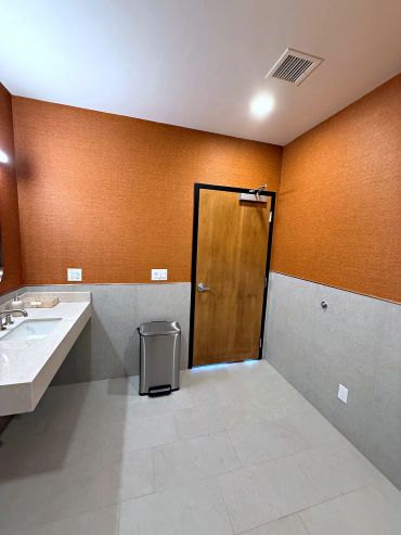 Orange textured vinyl wallcovering above grey tile wainscot in a commercial restroom in Arizona