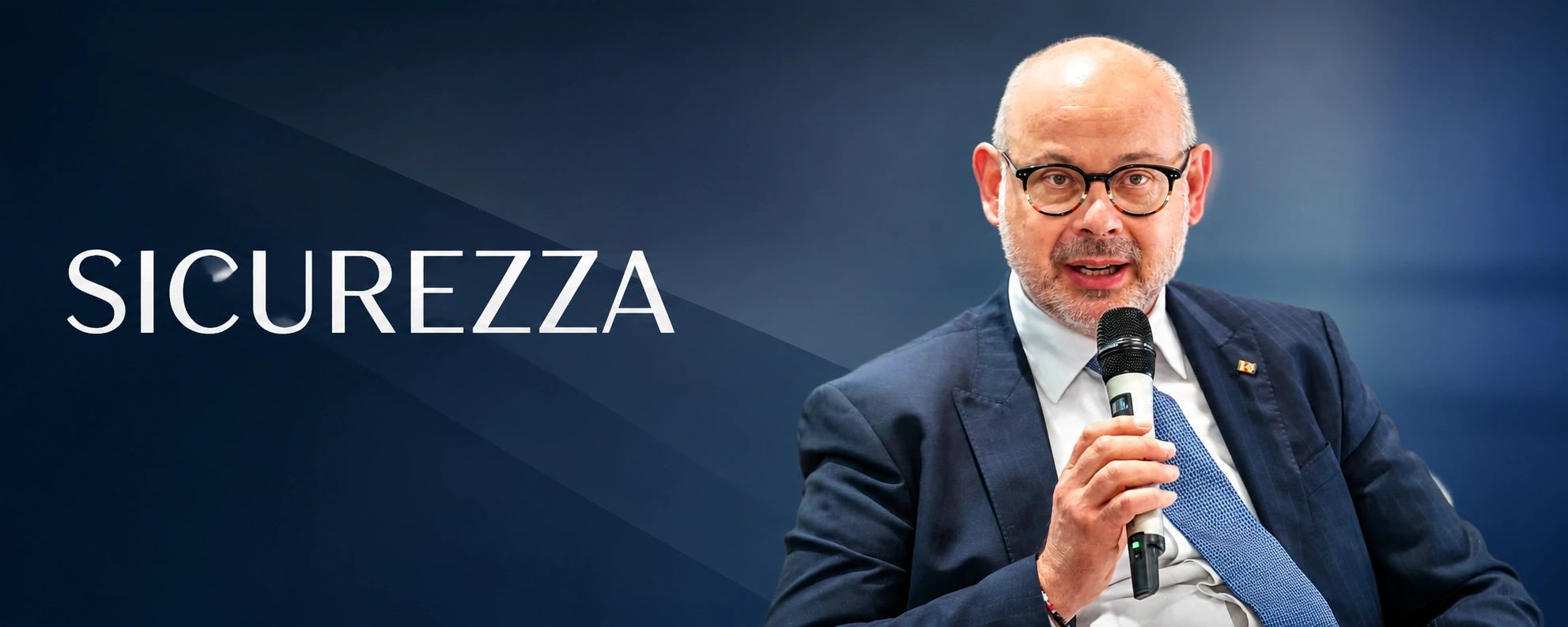 Uomo con microfono e scritta "SICUREZZA" sullo sfondo.