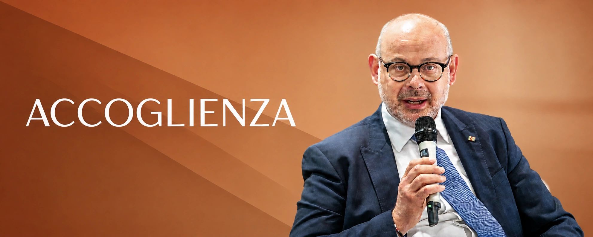 Uomo che parla con microfono con sfondo con la scritta "Accoglienza".