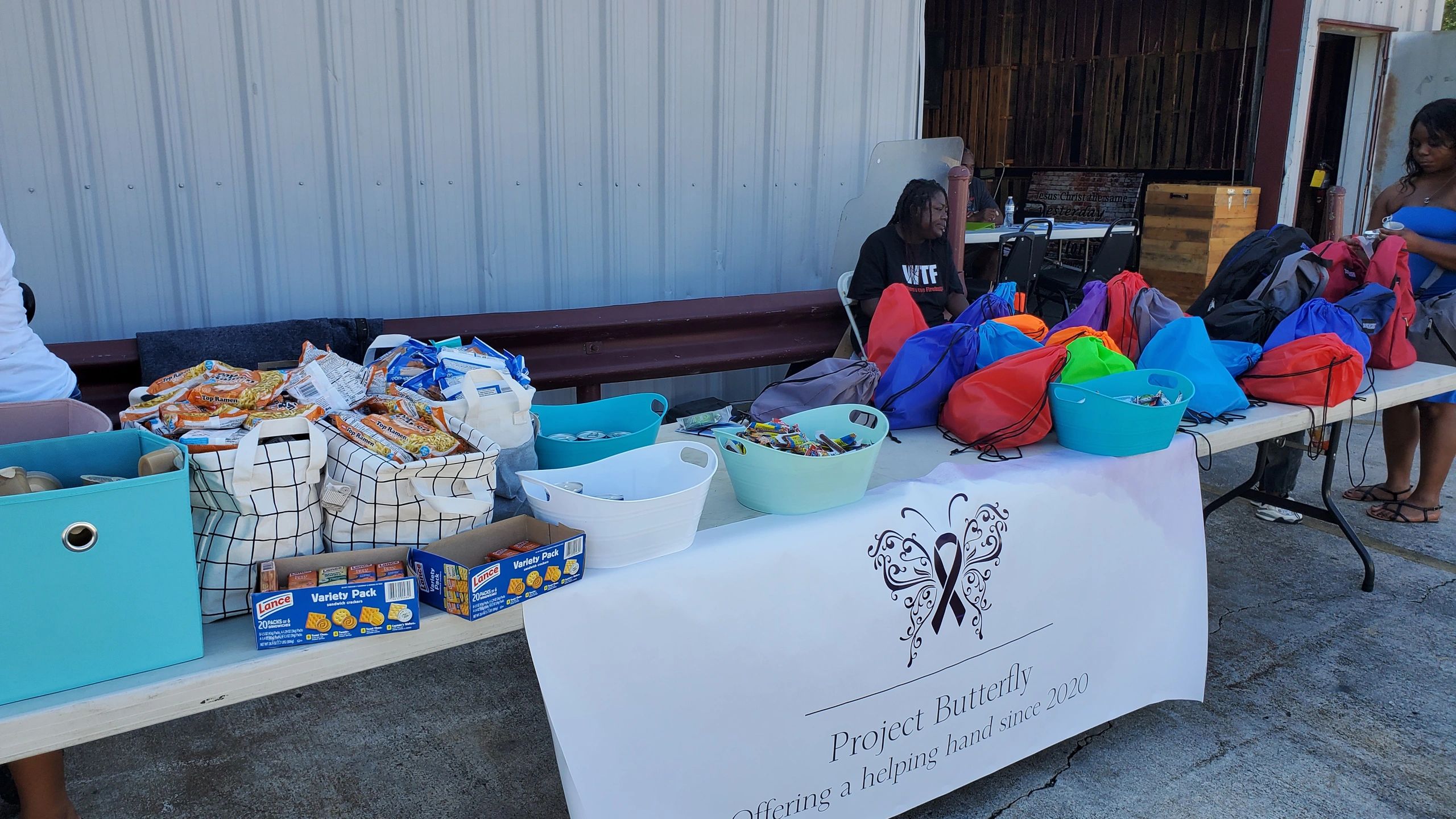 A community outreach table with snacks and colorful bags labeled Project Butterfly.