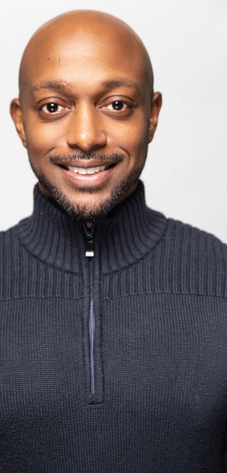 Smiling man wearing a dark knitted sweater with a zipper.