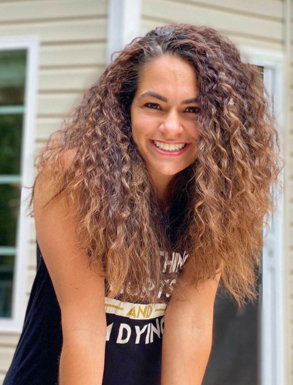 Smiling woman with voluminous curly hair in a casual outdoor setting.