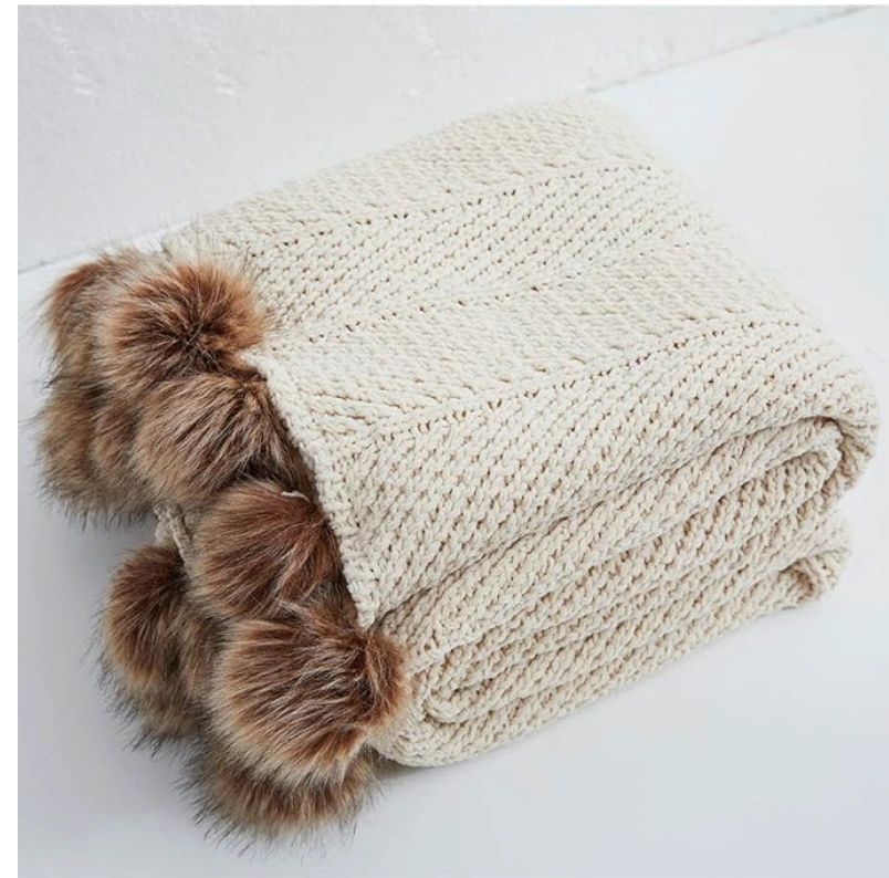 Beige knit throw blanket with pom poms.