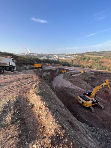 Construction site with multiple dump trucks and an excavator under clear blue sky.