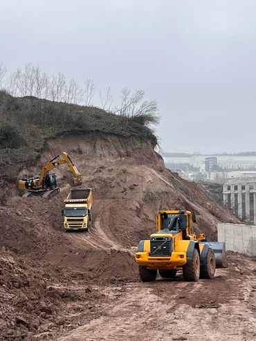 Heavy machinery working on a muddy construction site under a cloudy sky.