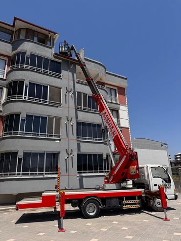 A red crane truck lifting a worker to a building roof for maintenance.