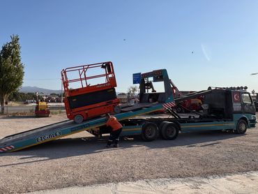 A truck loading an orange scissor lift on a sunny day.