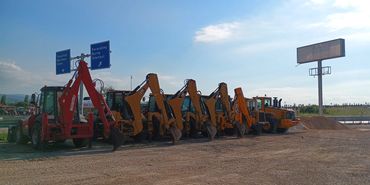 A lineup of construction excavators parked on a gravel lot under a clear sky.