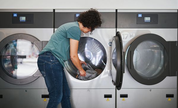 Woman loading clothes into industrial dryer at laundromat