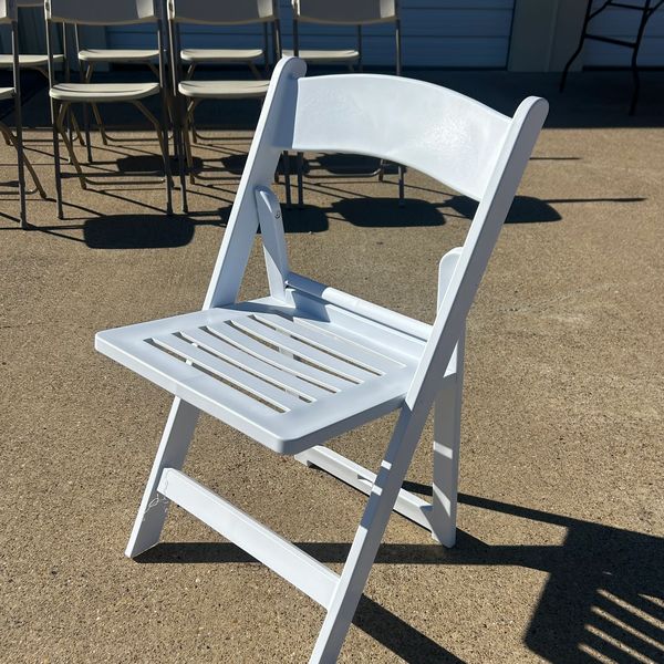 A single white folding chair on concrete with shadows.