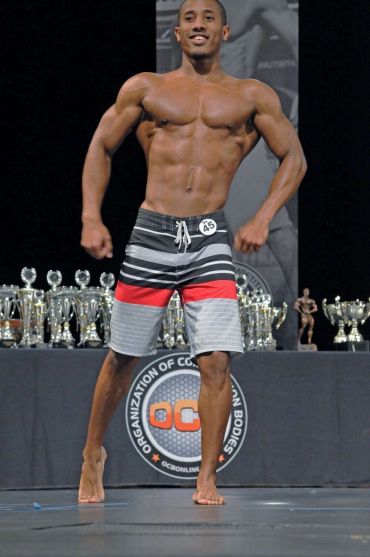Male bodybuilder posing in striped shorts at a competition.