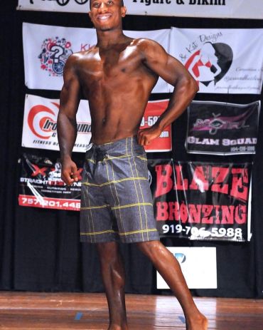 Man posing confidently on stage in checkered shorts.