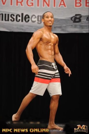 Man in striped shorts posing on stage at fitness event.