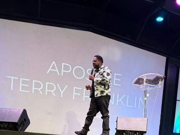 Apostle Terry Franklin speaking on stage with microphone.