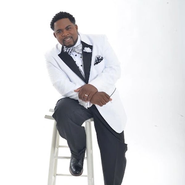 Man in white tuxedo sitting on a white stool.