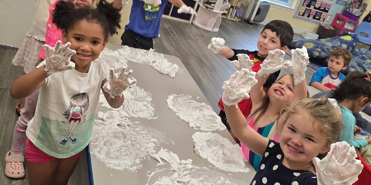 Kids smiling with hands covered in foam around a table.