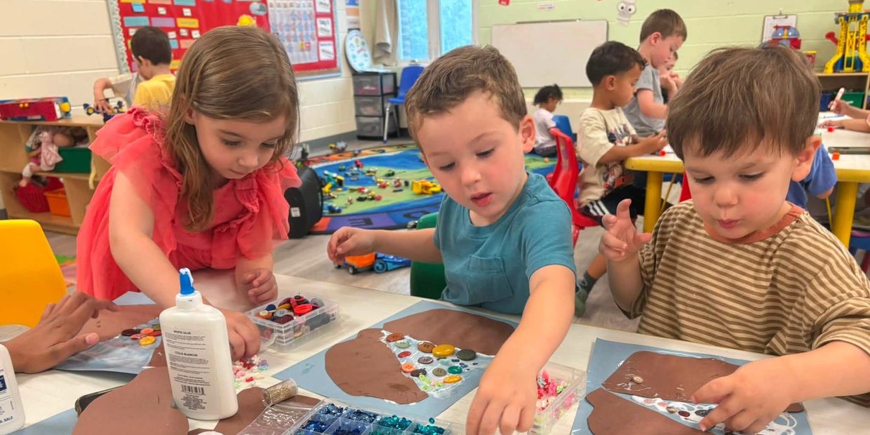 Three children crafting with buttons and glue in a classroom.