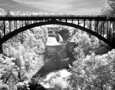 Black and white photograph of a steel arch bridge spanning a river and waterfall below.