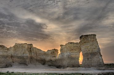 Color photograph of Monument Rocks with a natural arch opening at sunrise.