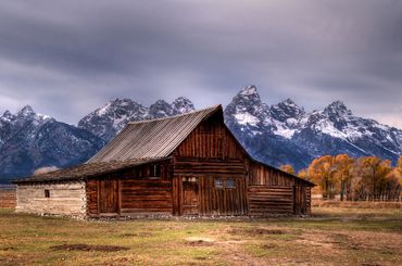 Color photograph of a rustic wooden barn with the Teton mountain range in the background.