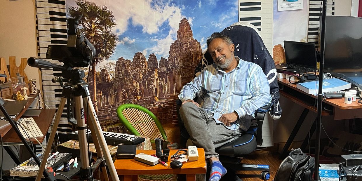 Man sitting in a cluttered room with camera and musical decor.